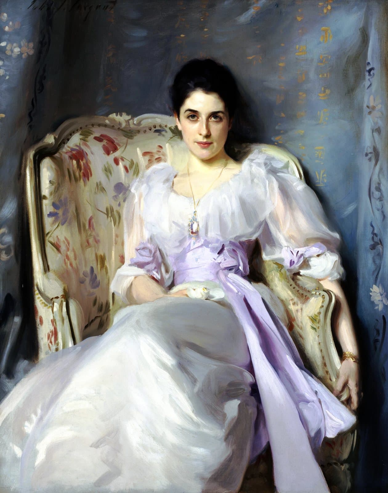 A woman in a white dress with a lilac sash, seated in a chair, looking directly at the viewer