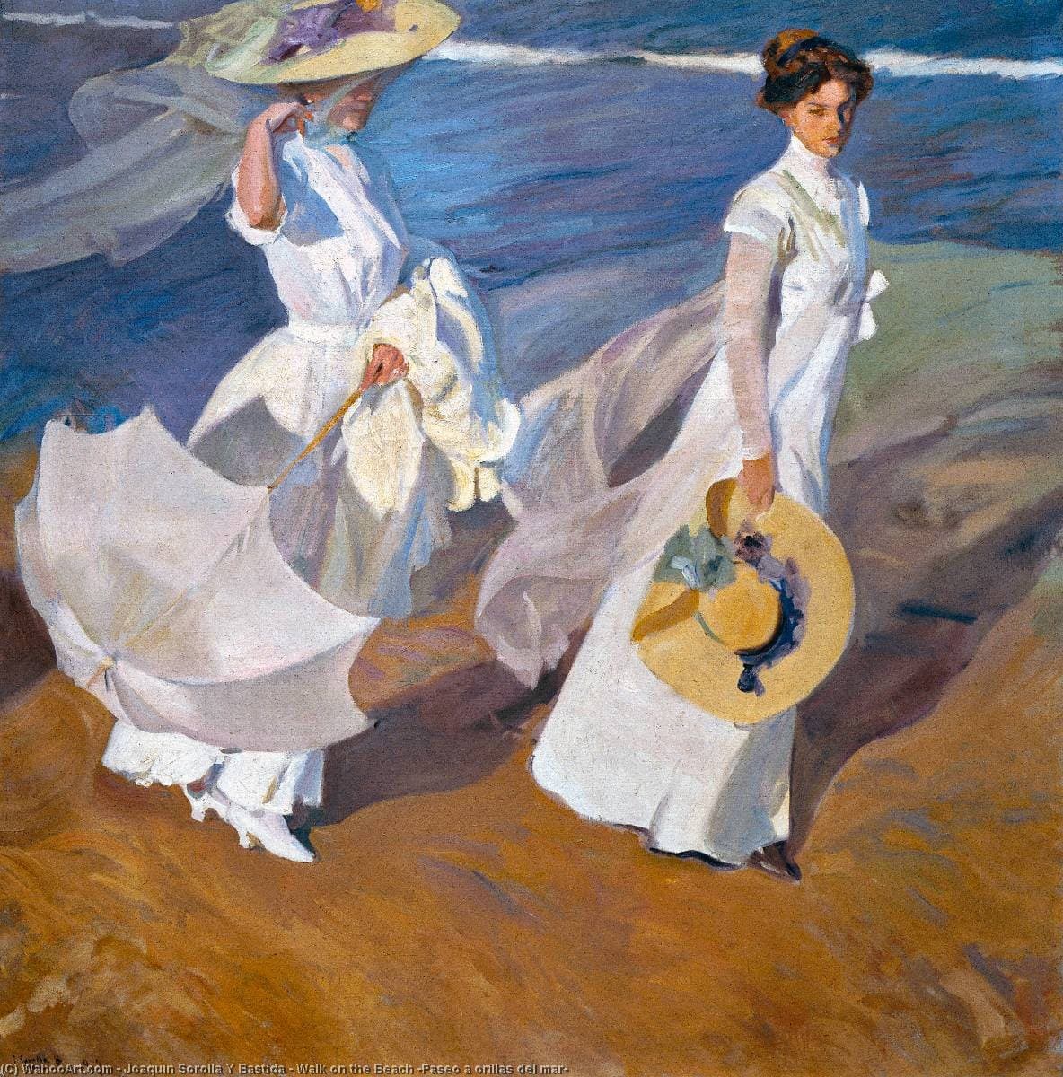 Two women in white dresses and hats walk along a bright beach, veils lifting in the wind