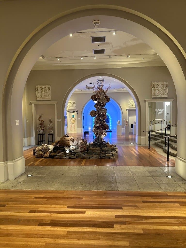 The arched galleries of the Coliseum of Art in sequence, with the found-object tower and a blue-lit archway beyond