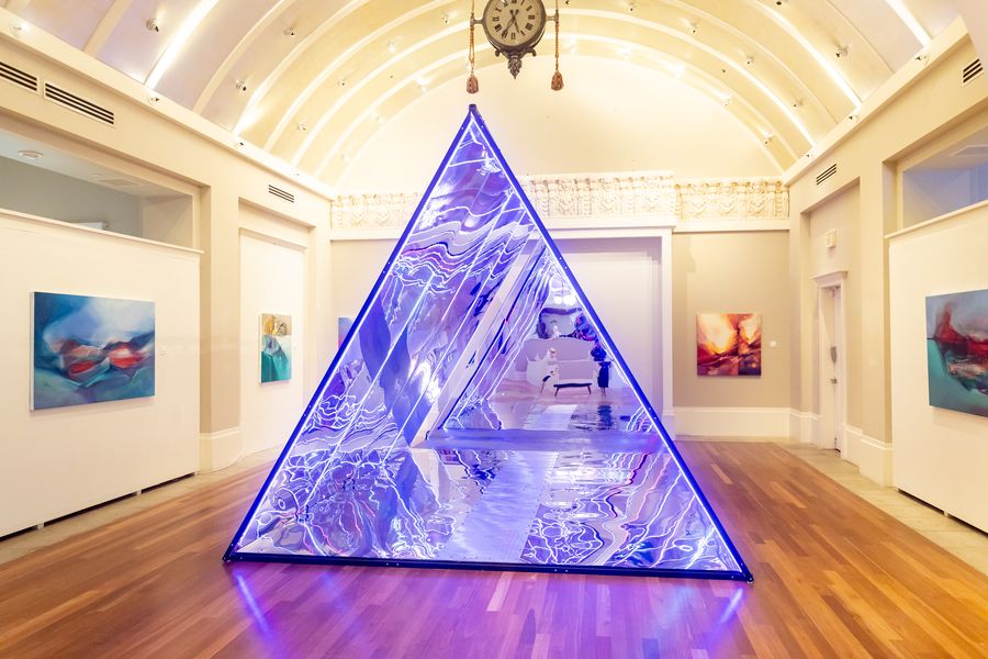 A glowing mirror-and-light pyramid under the barrel-vaulted, cream-and-gold hall, Coliseum of Art summer show. July 7, 2026.