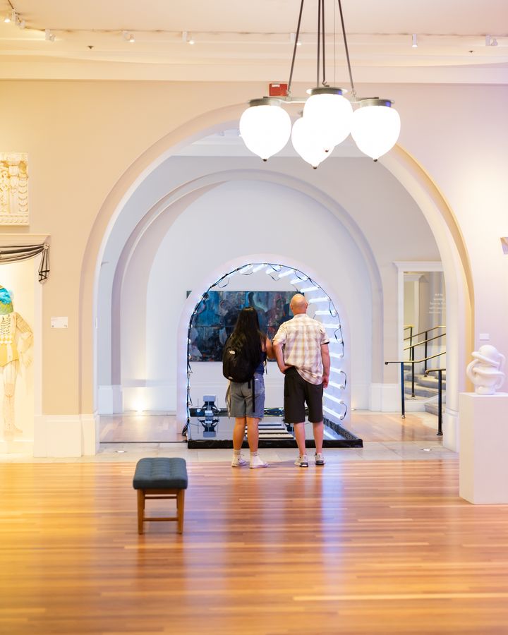 Two visitors walk through the nested arches toward an LED-lit portal. July 7, 2026.
